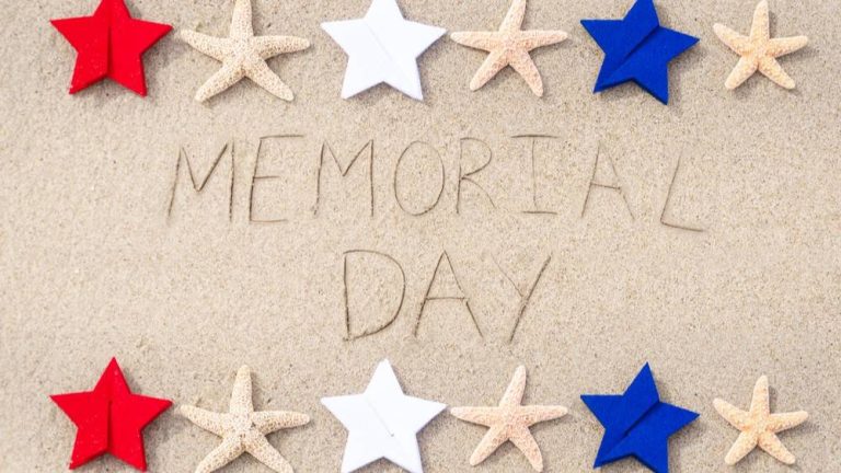 The words 'Memorial Day' written in the sand, bordered above and below by a row of alternating starfish and patriotic red, white, and blue stars.